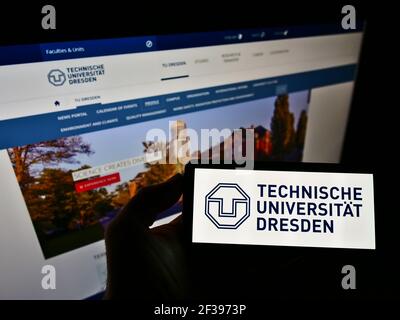 Person holding smartphone with logo of German university Technische Universität Dresden on screen in front of website. Focus on phone display. Stock Photo