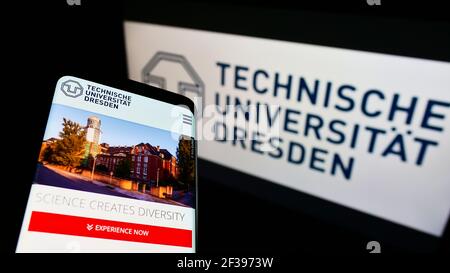 Cellphone with webpage of German education institution Dresden University of Technology on screen in front of logo. Focus on top-left of phone. Stock Photo