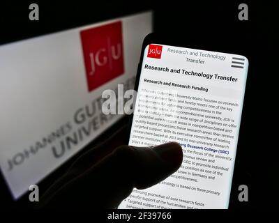 Person holding mobile phonewith webpage of German education institution University of Mainz on screen with logo. Focus on center of phone display. Stock Photo