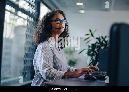 Female professional working on computer and talking on headset. businesswoman with headset working at her desk. Stock Photo