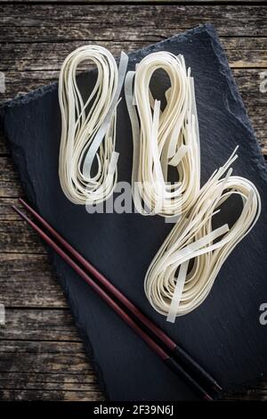 Dried white rice noodles. Raw pasta. Uncooked noodles on cutting board. Top view. Stock Photo