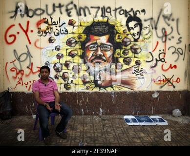 Protester opposing President Mohamed Morsi sits next to graffiti depicting Morsi on a wall in Cairo 1-Jul-2013. Stock Photo