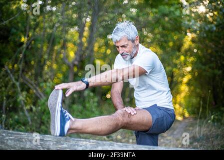 Mature man stretching his leg in forest Stock Photo