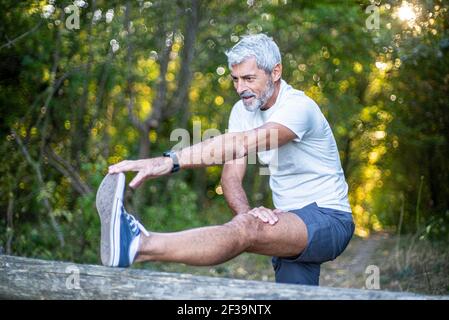 Mature man stretching his leg in forest Stock Photo
