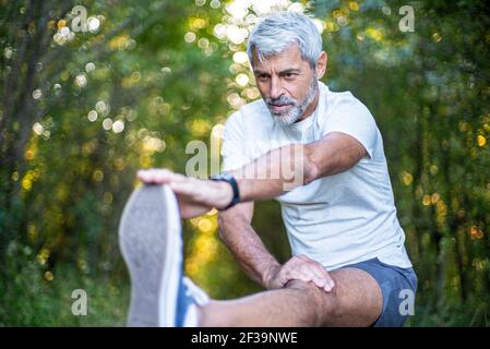 Mature man stretching his leg in forest Stock Photo