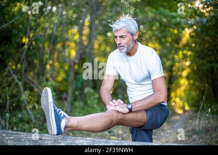 Mature man stretching his leg in forest Stock Photo