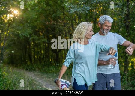 Smiling mature couple checking their smart watches in forest Stock Photo