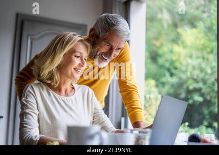 Smiling mature couple using laptop at home Stock Photo