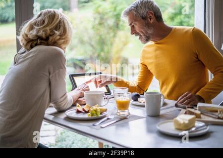 Mature couple using digital tablet while having breakfast at home Stock Photo