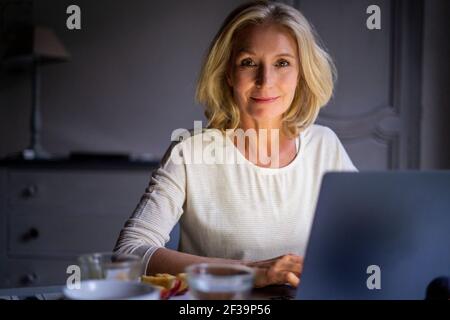 Portrait of smiling mature woman using laptop at home Stock Photo