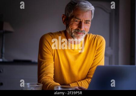 Smiling mature man using laptop at home Stock Photo