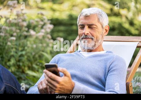 Smiling mature man using smartphone while sitting on deckchair Stock Photo