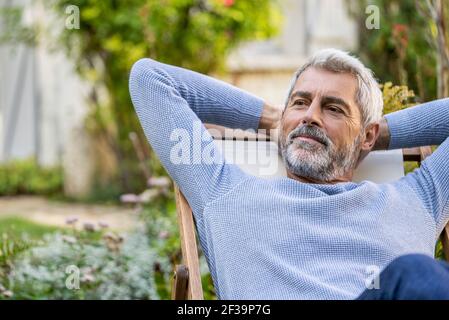 Thoughtful mature man with hands behind head sitting on deckchair Stock Photo
