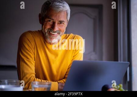 Portrait of smiling mature man using laptop at home Stock Photo