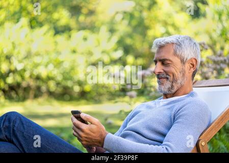 Smiling mature man using smartphone while sitting on deckchair Stock Photo