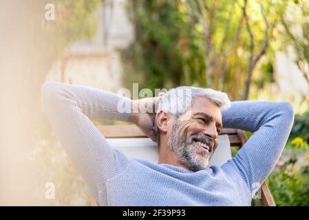 Smiling mature man with hands behind head sitting on deckchair Stock Photo