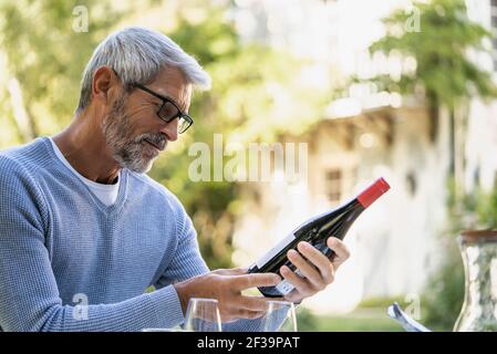 Mature man looking at wine bottle while sitting on chair Stock Photo