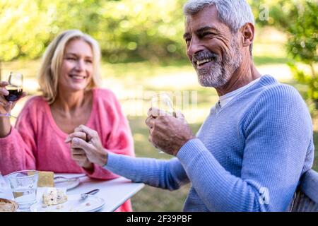 Smiling mature couple with holding hands drinking red wine in backyard Stock Photo