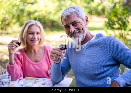 Portrait of smiling mature couple holding wine glasses while sitting at table Stock Photo