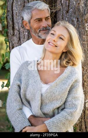 Thoughtful mature couple leaning on tree trunk Stock Photo