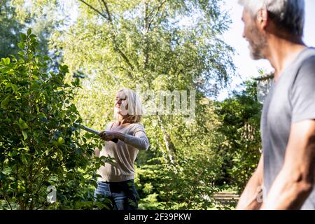 Smiling mature man looking at his wife pruning plant in backyard Stock Photo