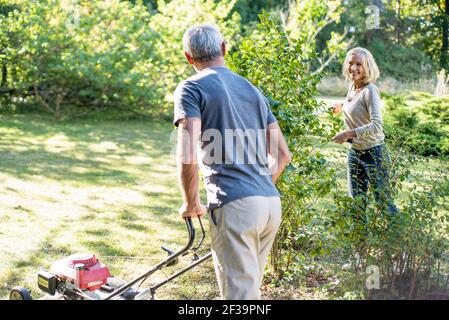 Happy mature couple mowing lawn and cutting plants in backyard Stock Photo