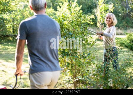 Happy mature couple mowing lawn and cutting plants in backyard Stock Photo