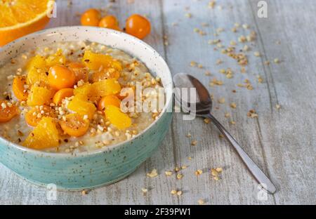 Breakfast oatmeal porridge with oranges and physalis served with roasted nuts in a bowl on a light wooden table with copy space Stock Photo