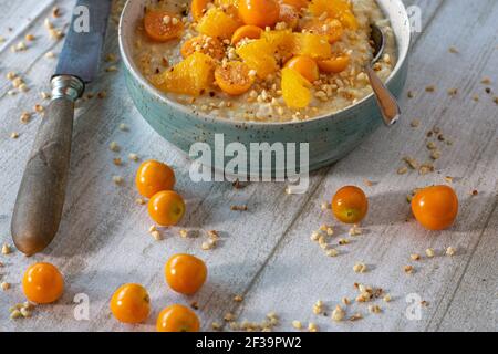 Oatmeal in a bowl with physalis and orange pieces served with roasted nuts on a wooden table with copy space Stock Photo