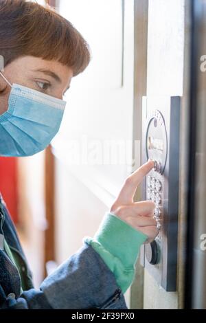 Woman wearing protective face mask entering password on security system Stock Photo