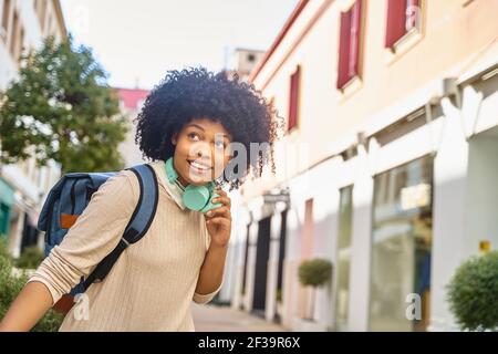 Smiling afro haired woman with headphones walking in city. Portrait of happy latina woman. High quality photo Stock Photo
