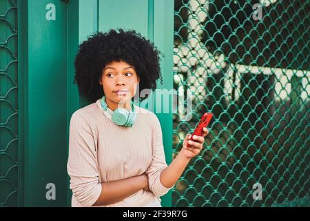 Afro-haired woman with headphones using smart phone on a green wall. Lifestyle concept. High quality photo Stock Photo