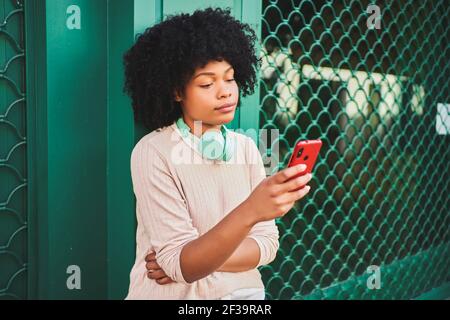 Afro-haired woman with headphones using smart phone on a green wall. Lifestyle concept. High quality photo Stock Photo