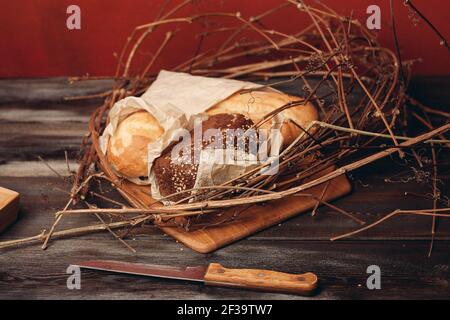 https://l450v.alamy.com/450v/2f39tw7/a-loaf-of-bread-lies-on-the-branches-of-the-nest-on-a-wooden-table-on-a-red-background-2f39tw7.jpg