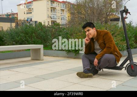 young boy smiling in a brown jacket sitting on his electric scooter. Stock Photo