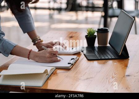 Business women using computer and calculator during note some data on notepad for calculate financial at cafe. Stock Photo