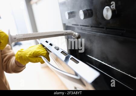 Gloved cleaner washing oven with steamer at home closeup Stock Photo