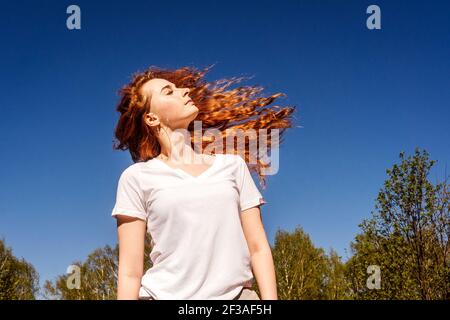 Young happy woman with flying long curly hair in sunshine. Sky background. Stock Photo