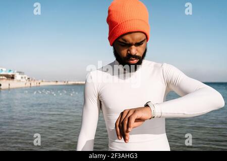 Handsome african american sportsman using smartwatch while working out at beach Stock Photo