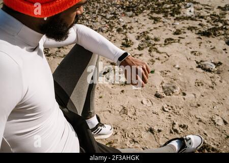 Handsome african american sportsman in earphones using smartwatch while working out at beach Stock Photo