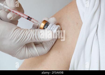 Open shoulder of the man before vaccination. Medical assistant preparing the syringe in the background. Stock Photo