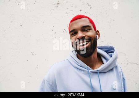 Happy african american guy in wireless earphones laughing at camera outdoors Stock Photo