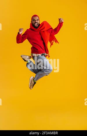 Excited happy african man wearing scarf having fun isolated over yellow background, full length, jumping Stock Photo