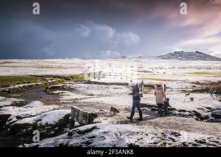 People enjoying walking in the snow on the wild rugged Rough Tor on Bodmin Moor in Cornwall. Stock Photo