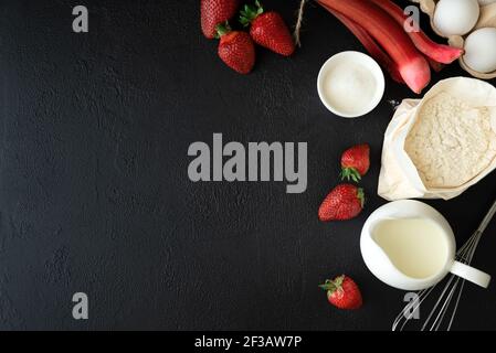 Baking background. Food ingredients for baking: flour, eggs, sugar, milk and berries on dark background. Flat lay. Copy space. Top view Stock Photo