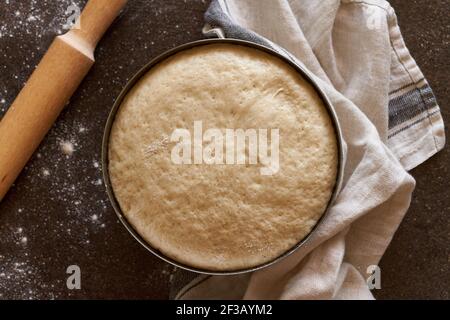Raw yeast dough resting and rising in large metal bowl with linen towel  Stock Photo
