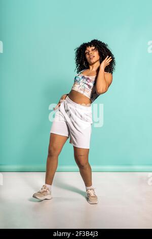 Stock photo of beautiful african woman with curly hair dancing in studio shot against blue background. Stock Photo