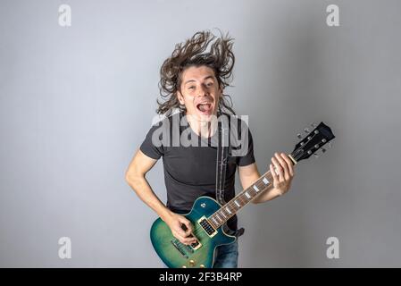 A young man is playing an electric guitar singing and waving his long hair. Emotional performance of rock and roll Stock Photo