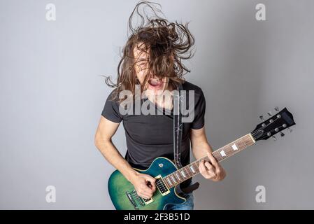 A young man is playing an electric guitar singing and waving his long hair. Emotional performance of rock and roll Stock Photo