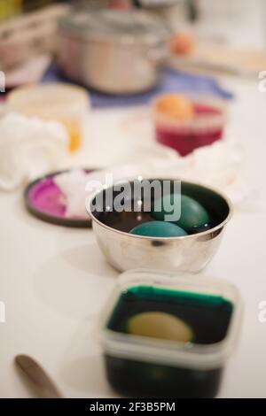 Colourful eggs in dye in plastic and metal bowls on a messy kitchen surface, family traditions for Easter Stock Photo